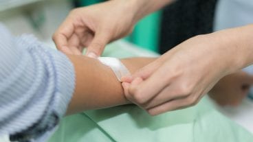 Nurse applying bandage on patient's hand after blood test in hospital.