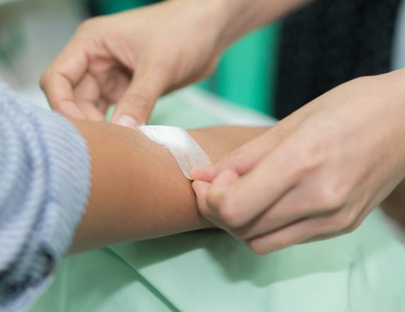 Nurse applying bandage on patient's hand after blood test in hospital.