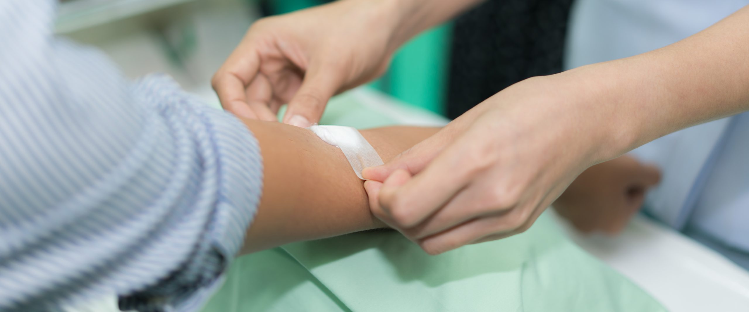 Nurse applying bandage on patient's hand after blood test in hospital.