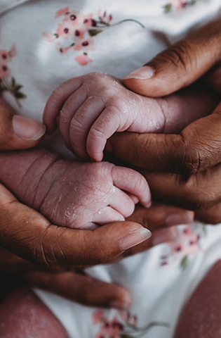 Ethnic female hands holding tiny waxy hands of multiracial newborn