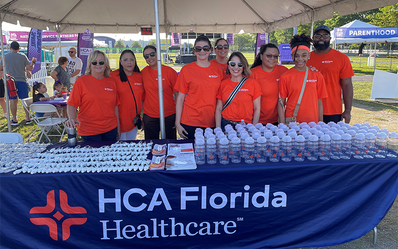Group of people wearing orange shirts in front of a table with banner that says HCA Florida Healthcare at a March for Babies event